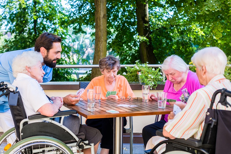 Group of seniors and nurse playing cards in rest home